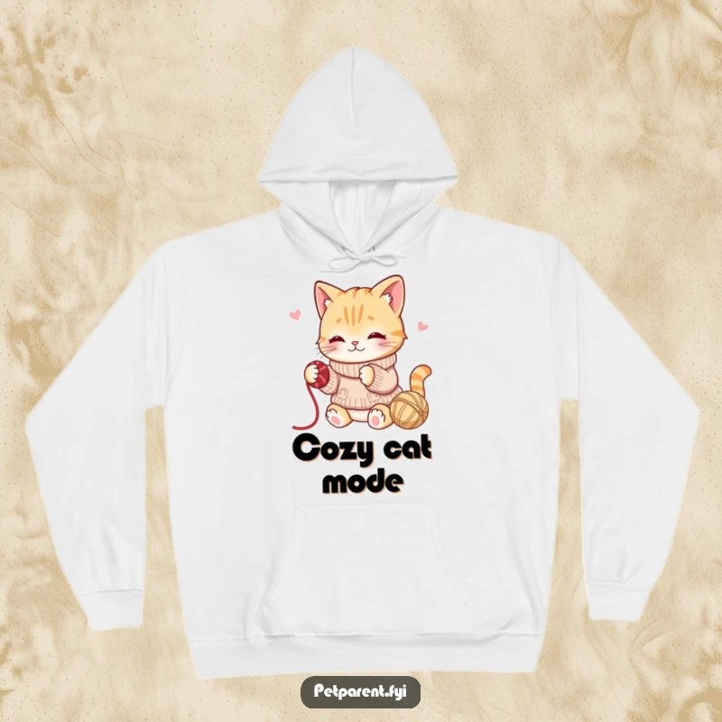 Funny hoodie showcasing a playful cat in a sweater batting a ball of yarn, radiating cozy fun.